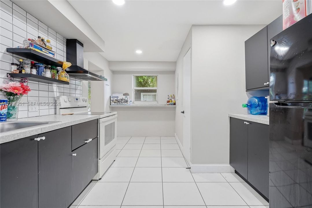 Kitchen featuring matte dark cabinetry, white tiled backsplash, light-toned countertops, recessed lighting, and tile flooring