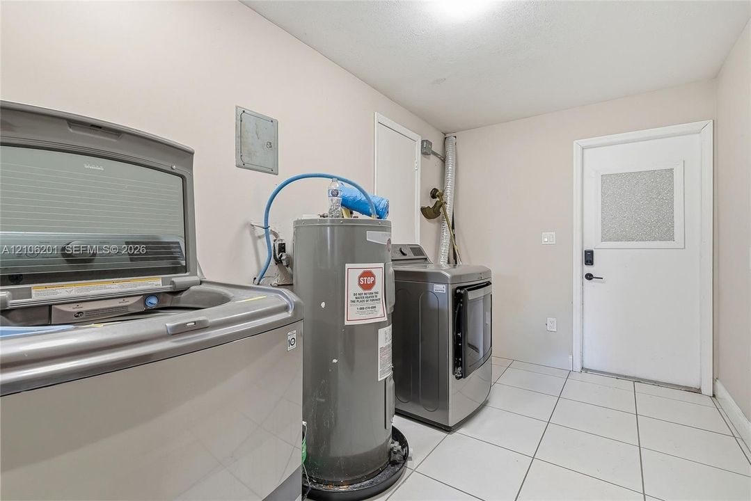 Utility room featuring large-format ceramic tile flooring, a dedicated water heater, and an exterior door with a decorative glass panel