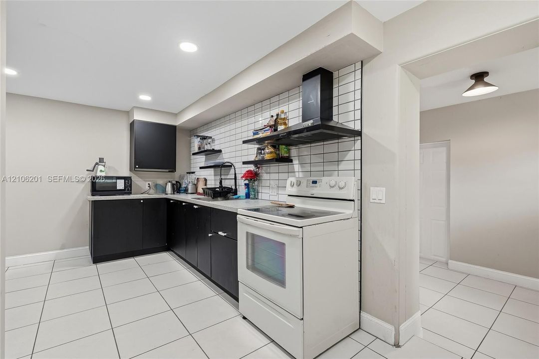 Kitchen featuring matte black cabinetry, white square tile backsplash, white ceramic tile flooring, built-in black range hood, and recessed lighting