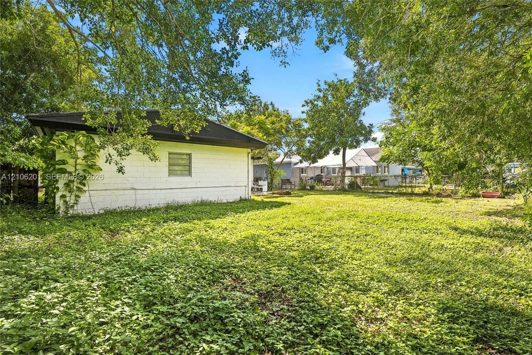 Expansive backyard featuring a block-constructed outbuilding, mature tree canopy, and perimeter fencing