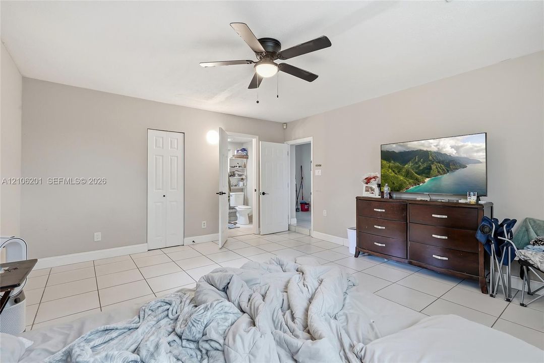 Neutral-toned room featuring ceramic tile flooring, a central ceiling fan with integrated lighting, and multiple interior hinged doors