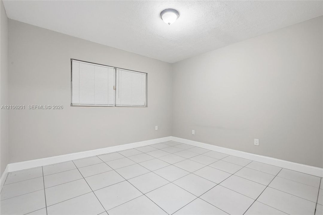 Neutral-toned interior room featuring large-format ceramic tile flooring, a dual-pane horizontal sliding window, and a ceiling-mounted flush light fixture