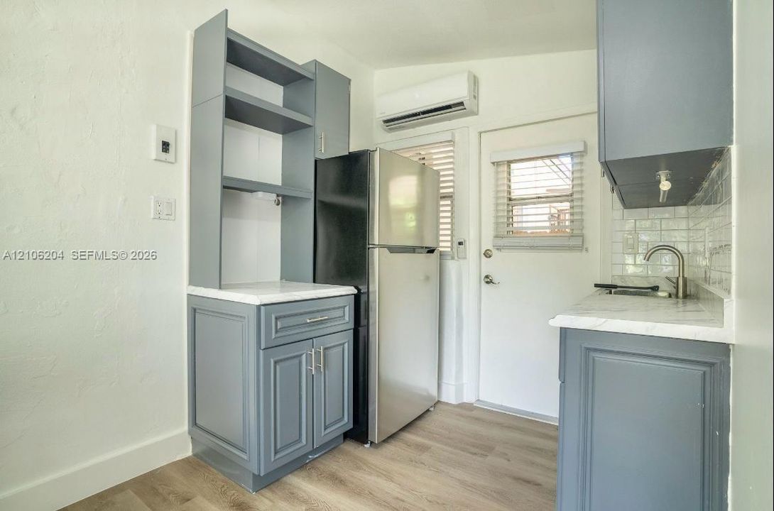 Kitchen featuring gray shaker-style cabinetry, white countertops, light-toned wood-finish flooring, stainless steel refrigerator, and wall-mounted climate control unit