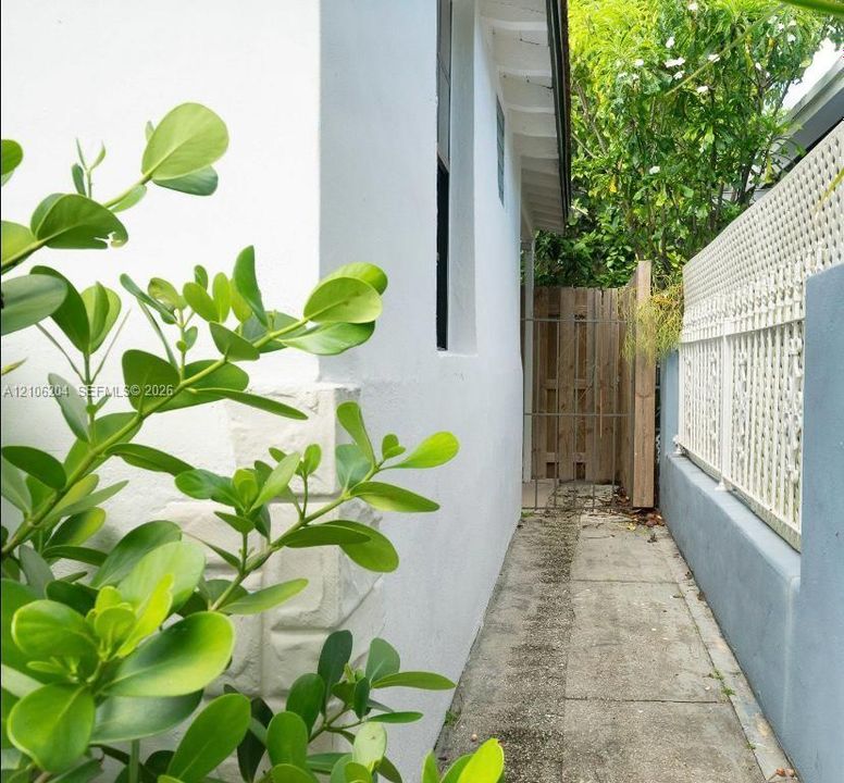 Exterior side path featuring white stucco wall, concrete walkway, decorative lattice fencing, and wooden privacy gate