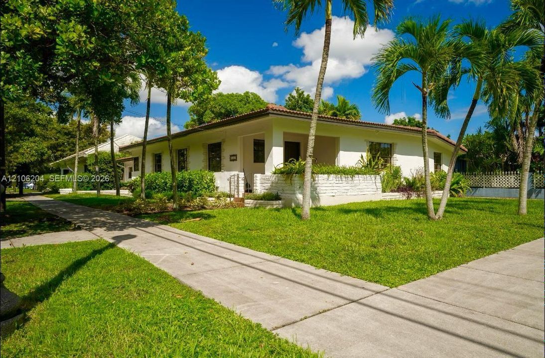 Single-story residence featuring a painted brick facade, a covered front entry, low-profile tiled roofing, and a manicured lawn with mature palm trees