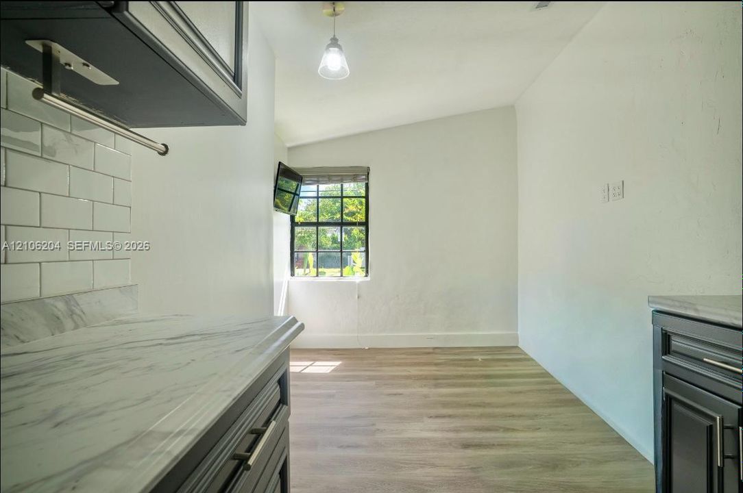 Kitchen featuring dark cabinetry, stone-finish countertops, white subway tile backsplash, wood-finish flooring, and a multi-pane window