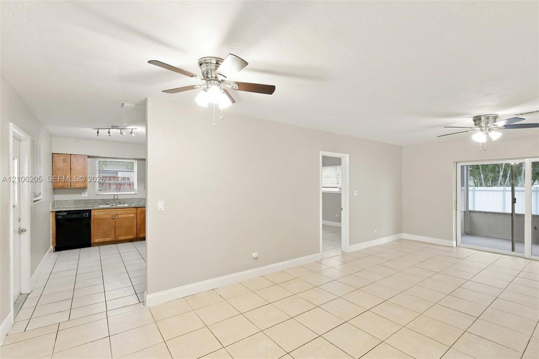 Open-concept interior featuring light-toned tile flooring, dual ceiling fans, sliding glass doors, and a kitchen equipped with wood-finish cabinetry and stone-surface countertops