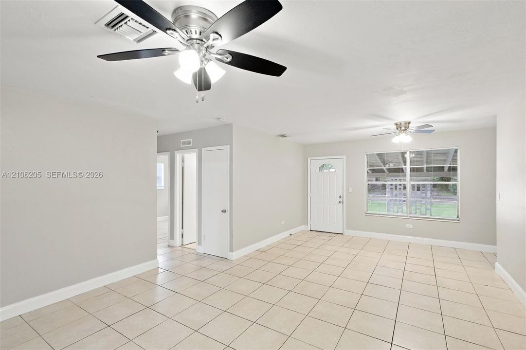 Interior space featuring large-format neutral floor tile, dual ceiling fans with integrated lighting, a solid-core exterior door with a decorative glass insert, and a wide-pane window