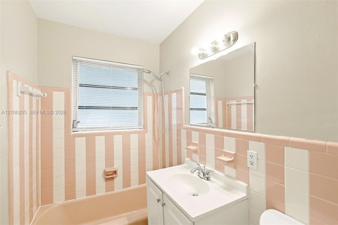 Wall-mounted vanity with a porcelain sink and chrome faucet, rectangular wall mirror, three-light vanity fixture, and full-height striped ceramic wall tiling surrounding the porcelain bathtub