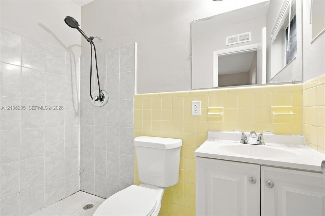 Bathroom featuring a white vanity cabinet, ceramic tile walls, a wall-mounted mirror, and a shower head with an adjustable hose