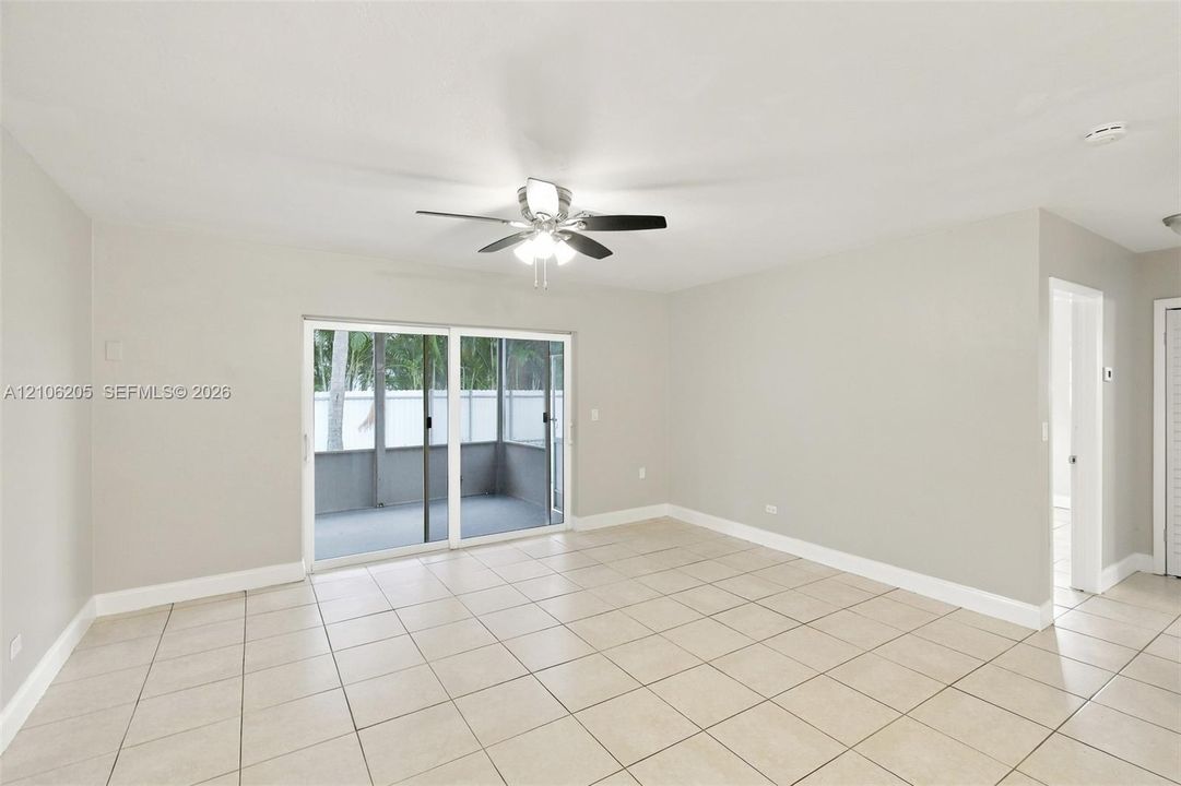 Neutral-toned interior featuring ceramic tile flooring, a multi-blade ceiling fan with integrated lighting, and a sliding glass door providing external access to a screened enclosure