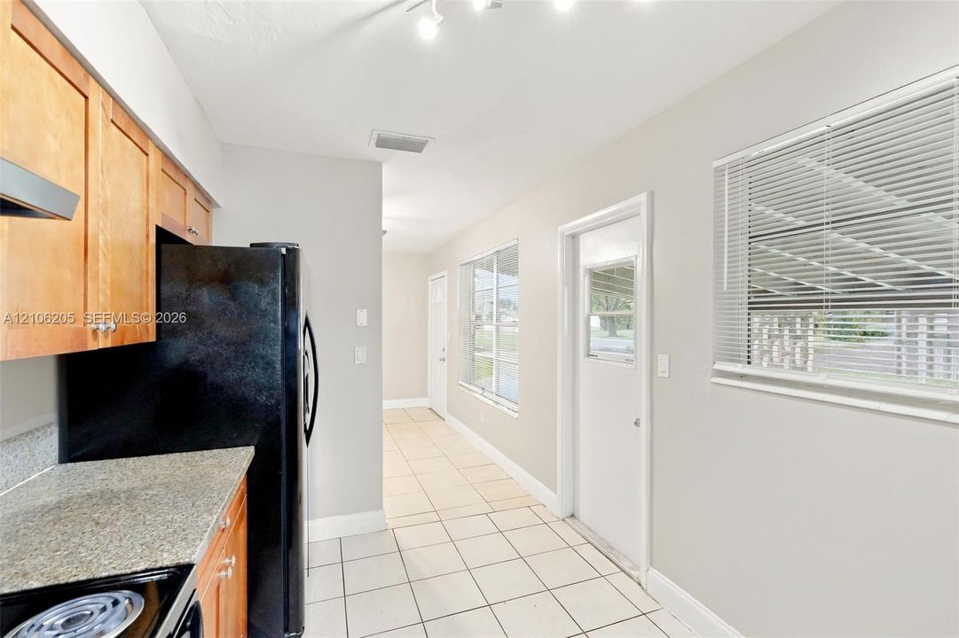 Kitchen featuring natural finish wood cabinetry, stone-texture countertops, ceramic tile flooring, and multiple exterior-access doors