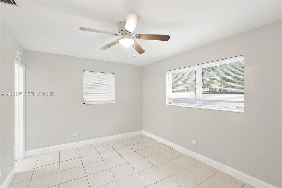 Neutral-toned interior featuring large-format tile flooring, a multi-blade ceiling fan with integrated lighting, and dual windows