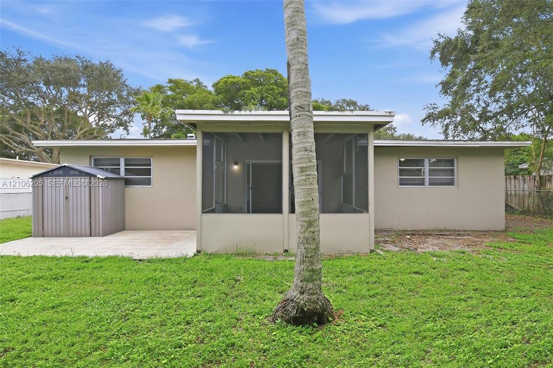 Exterior rear elevation featuring a screened-in lanai, concrete patio, and detached metal storage structure situated on a grass-covered lot