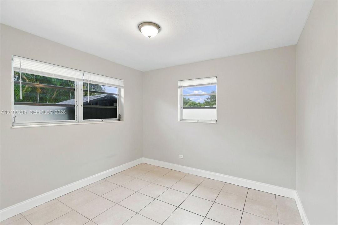 Neutral-toned interior featuring large windows with horizontal blinds, overhead flush-mount lighting, and light-colored tile flooring