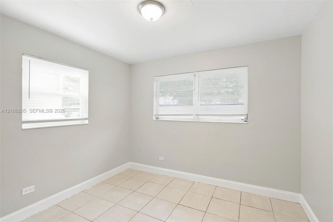 Neutral-toned walls, square tile flooring, two multi-pane windows with horizontal blinds, and a central ceiling-mounted light fixture
