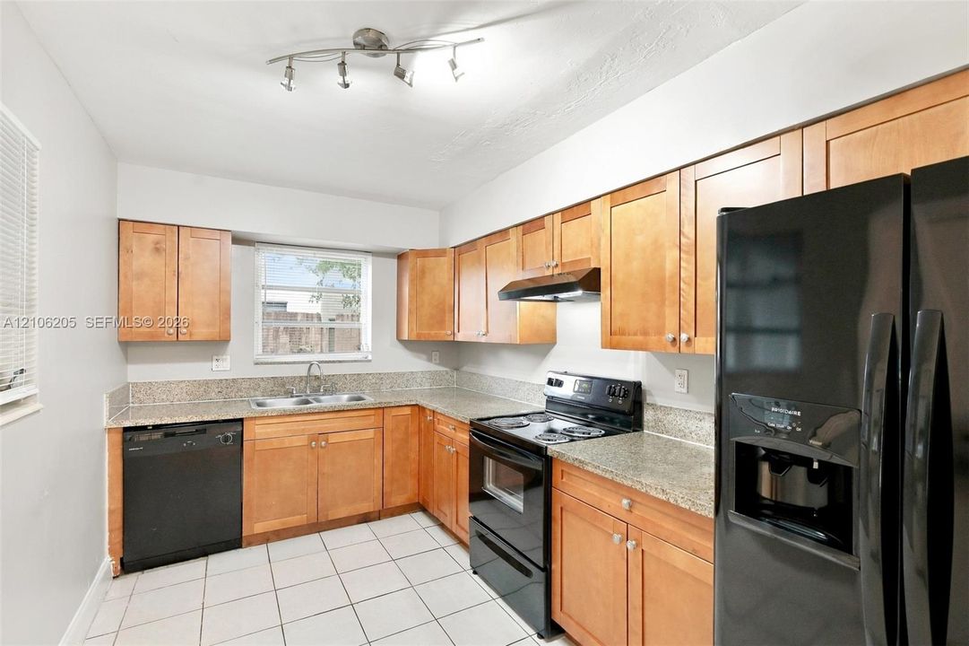 Kitchen featuring wood cabinetry, stone-finish countertops, black appliances, a double-basin stainless steel sink, and tile flooring
