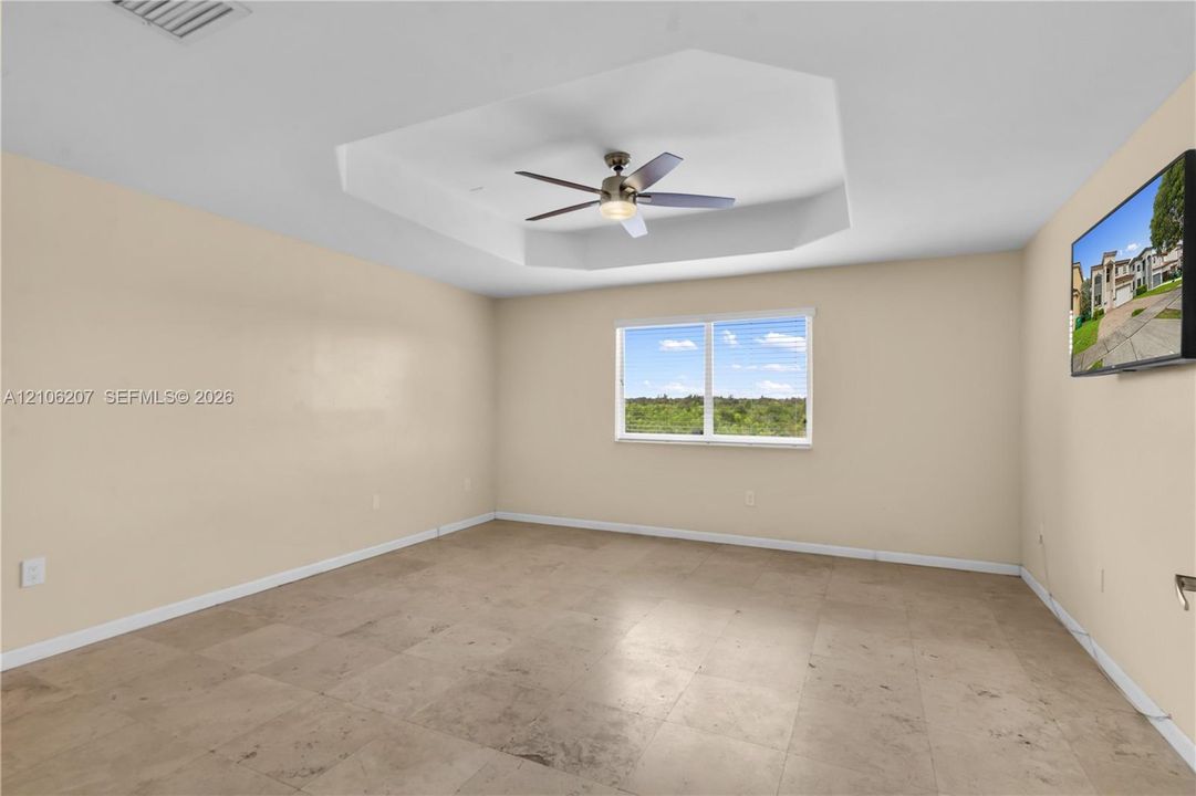 Interior room featuring a tray ceiling with a multi-blade ceiling fan and light fixture, stone-finish tile flooring, and a window with exterior landscape imagery