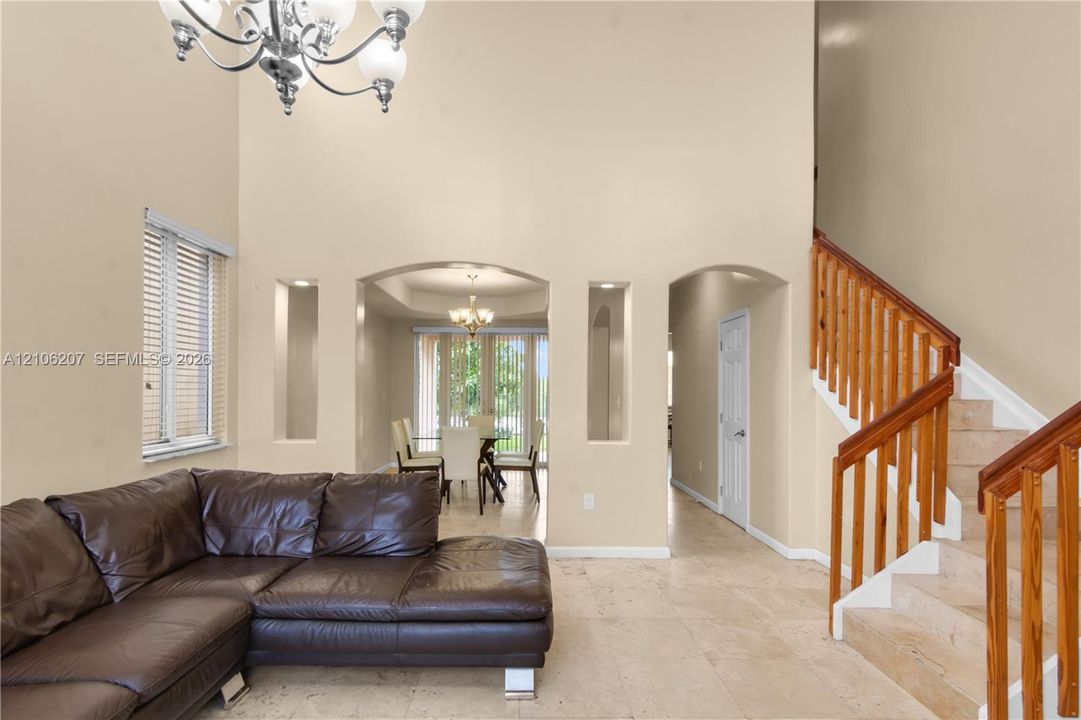 High ceilings with a decorative chandelier, arched wall niches, neutral stone-finish flooring, and a wooden staircase railing