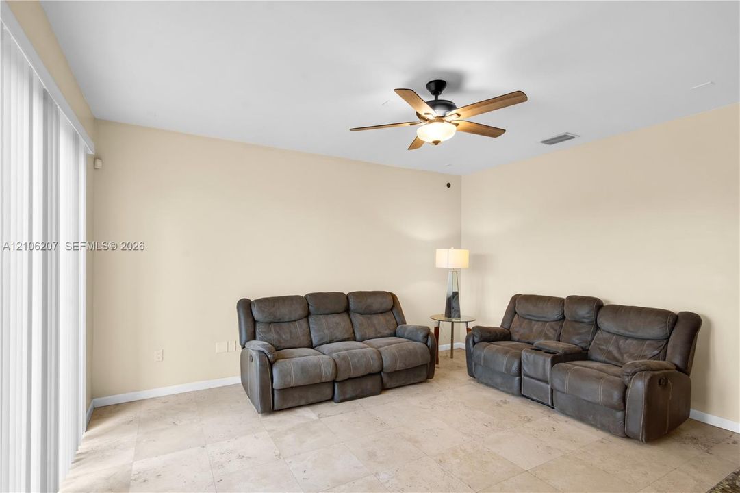 Neutral-toned living space featuring large-format tile flooring, a central ceiling fan with integrated lighting, and full-height sliding glass doors