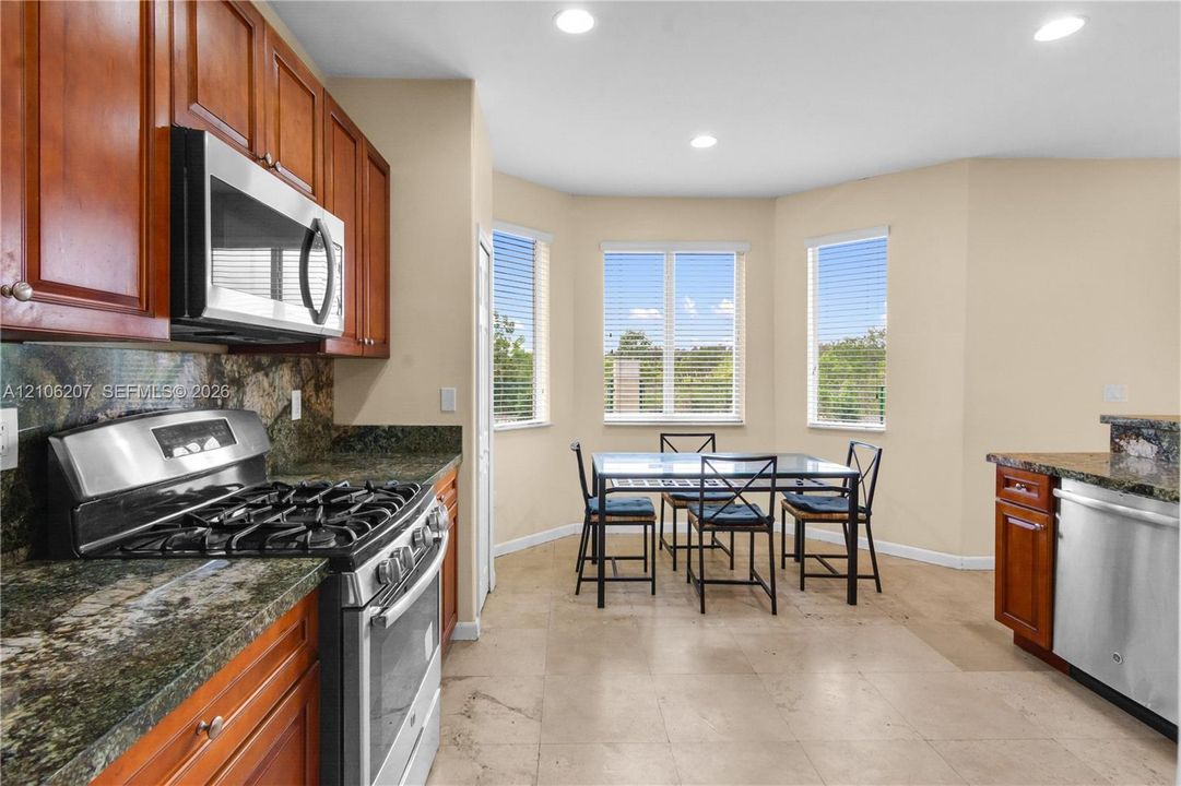 Kitchen featuring wood cabinetry, stone countertops, stainless steel gas range, built-in microwave, and tile flooring