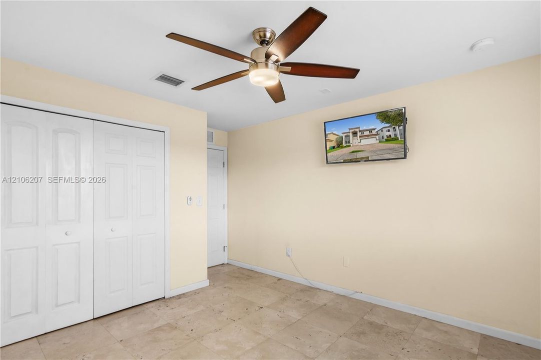 Neutral-toned walls featuring stone-finish floor tiling, five-panel sliding closet doors, and a central ceiling fan with an integrated light fixture