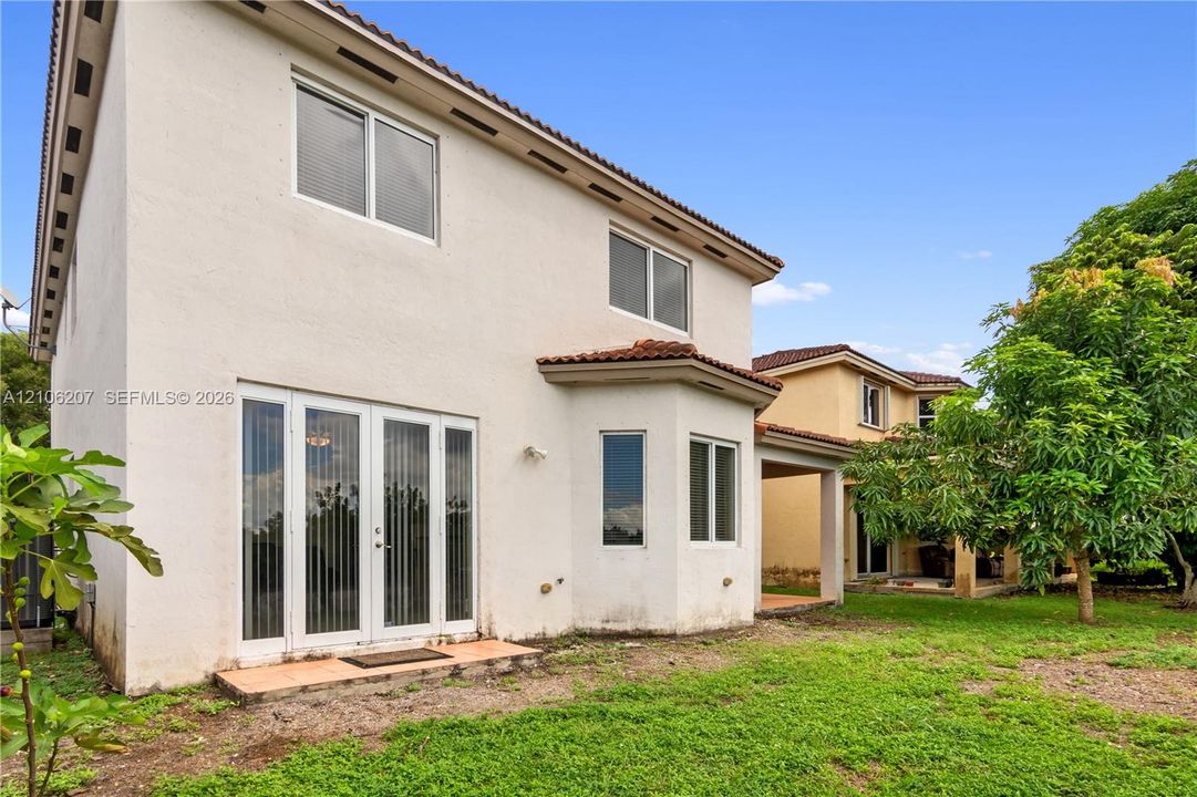 Stucco exterior with a multi-level roofline, clay tile accents, bay window configuration, and glass-paneled double doors opening to the grounds
