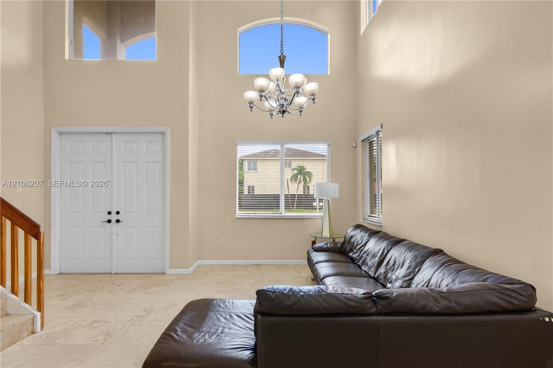 Double-height ceilings, arched transom windows, tile flooring, multi-light chandelier, and double-door entry