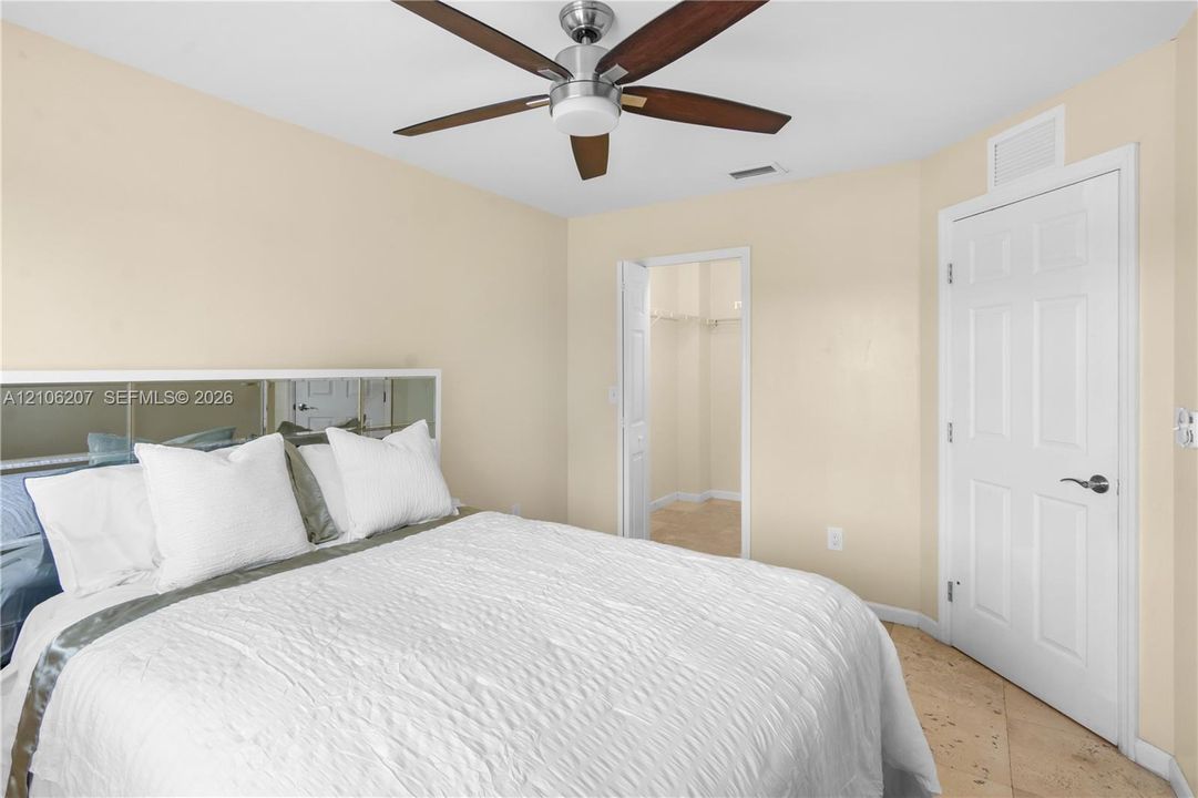 Room featuring tile flooring, a mirrored headboard accent, a six-blade ceiling fan with integrated lighting, and a six-panel interior door