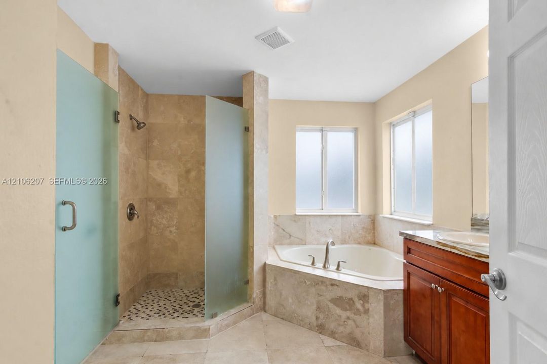 Bathroom featuring a corner soaking tub, walk-in shower with frosted glass enclosure, stone-tile surround, vanity with stone countertop, and an integrated undermount sink
