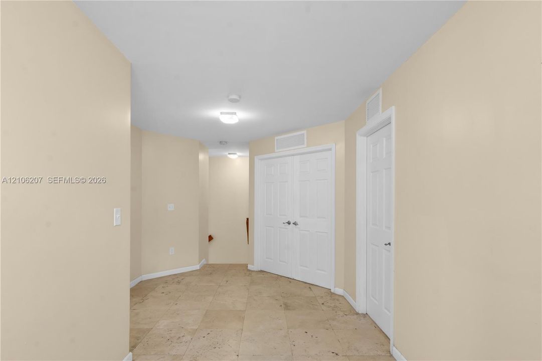 Neutral-toned interior space featuring stone-tile flooring, white six-panel closet doors, single-panel interior door, and flush-mount ceiling lighting