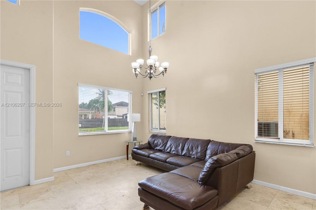 Two-story vaulted ceiling featuring a multi-light chandelier, arched accent window, stone flooring, and large picture windows
