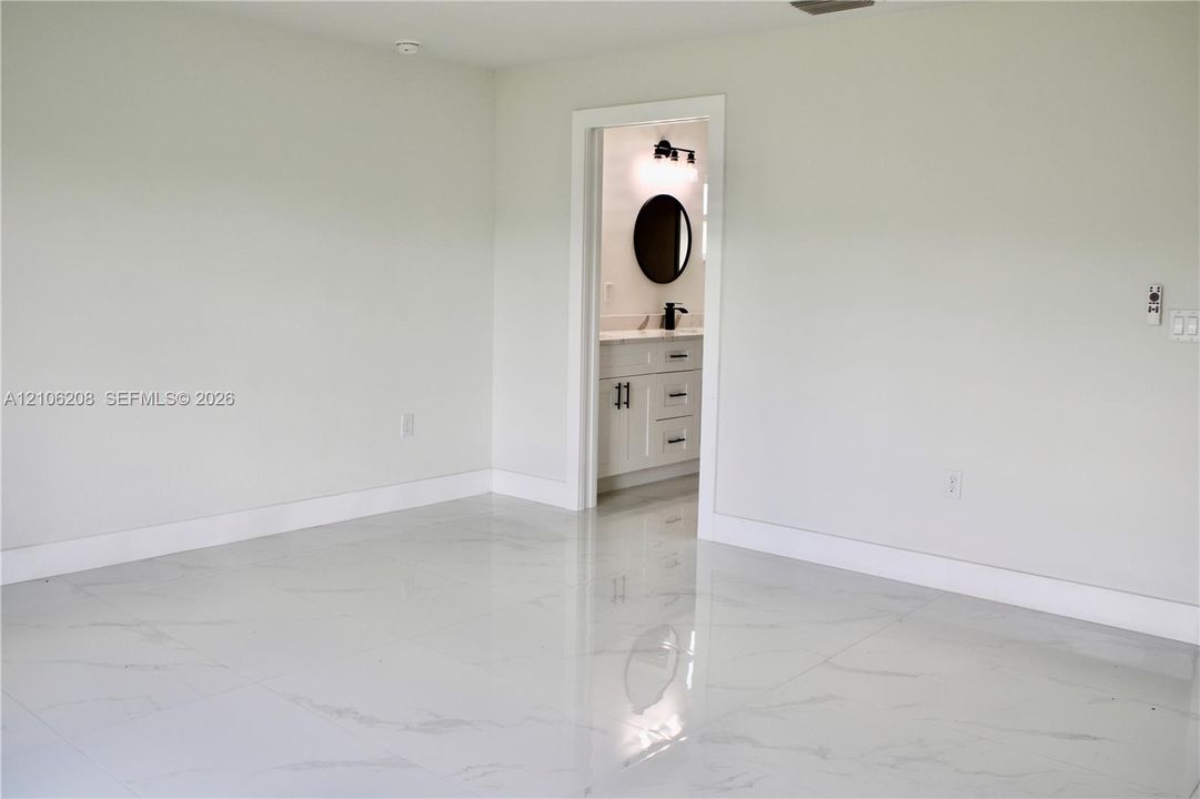 Large-format tile flooring with a stone-finish pattern, paired with a vanity featuring a light-toned countertop, undermount sink, circular wall mirror, and matte black hardware