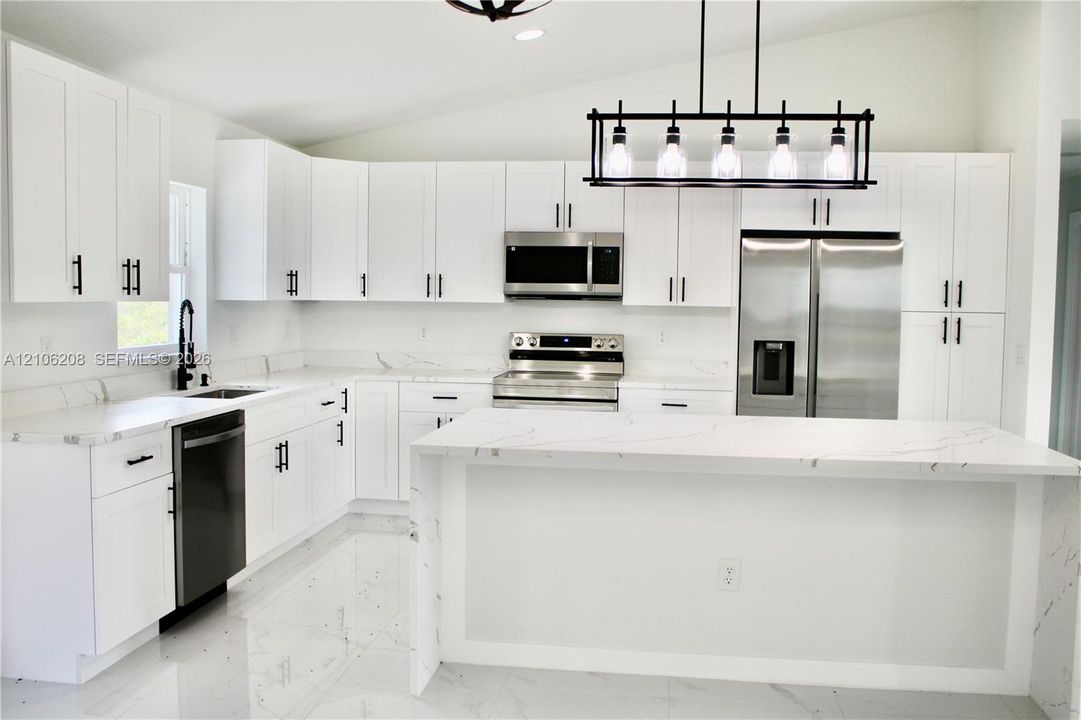 Kitchen featuring white cabinetry with matte black hardware, stone-patterned countertops, a central island, stainless steel appliances, and a linear pendant light fixture