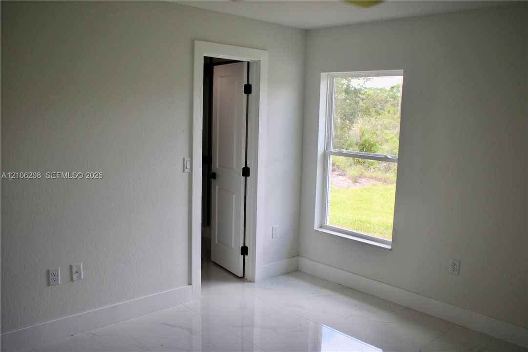 Neutral-toned interior room featuring large-format tile flooring, a single-hung window with natural lighting, and a solid-core interior door with matte black hardware