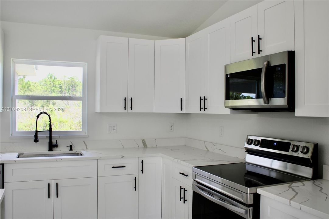 Kitchen featuring white Shaker-style cabinetry, stone-patterned countertops, stainless steel appliances, and a high-arch matte black faucet