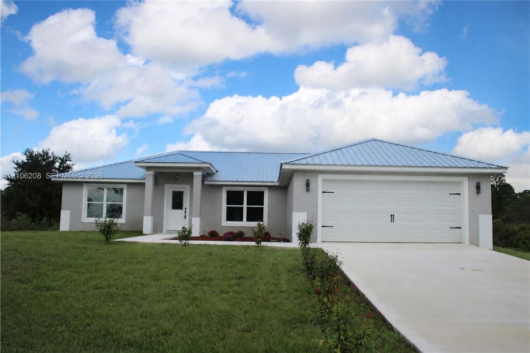 Single-story exterior featuring a metal roof, stucco finish with corner quoins, two-car garage, and concrete driveway