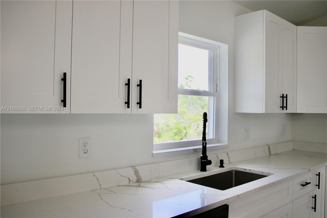 White shaker-style cabinetry with matte black pulls, light-toned stone-finish countertops with veining, under-mount stainless steel sink, and a matte black gooseneck faucet
