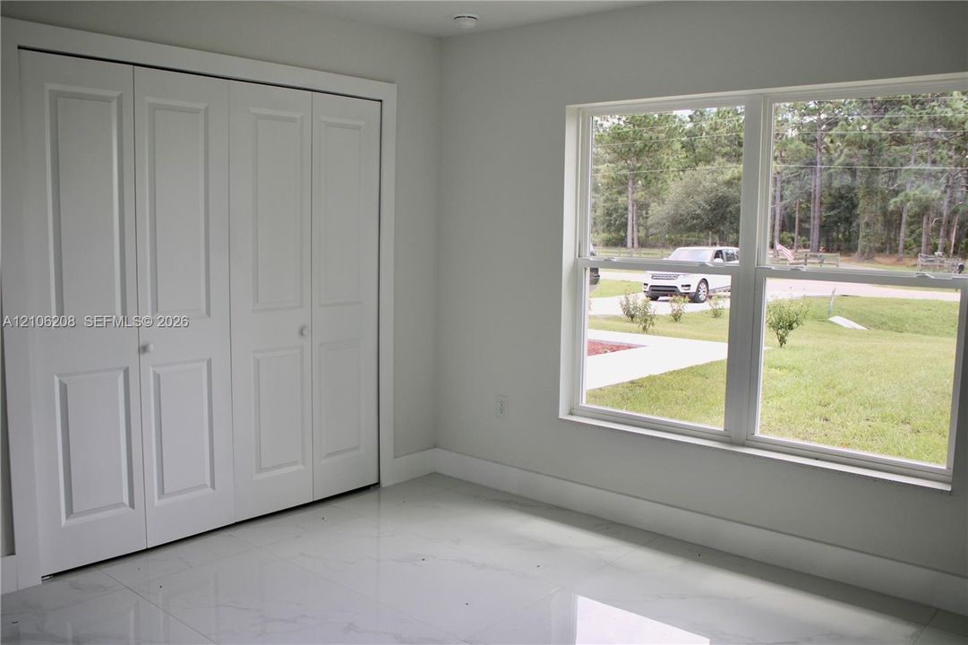 Room with polished tile flooring, white interior finishes, multi-panel closet doors, and large dual-pane windows