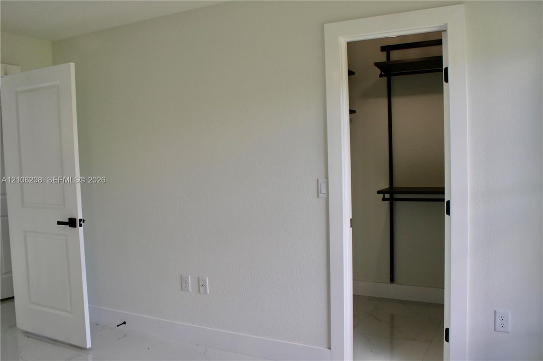 Walk-in closet featuring dark-finish built-in shelving, two-panel interior door with matte black hardware, and polished stone-finish tile flooring