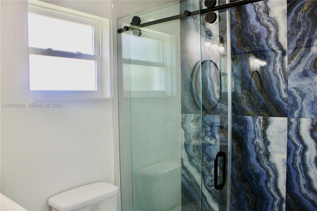 Shower enclosure featuring large-format blue-toned decorative wall tile, sliding frameless glass door with matte black hardware, and single-hung window