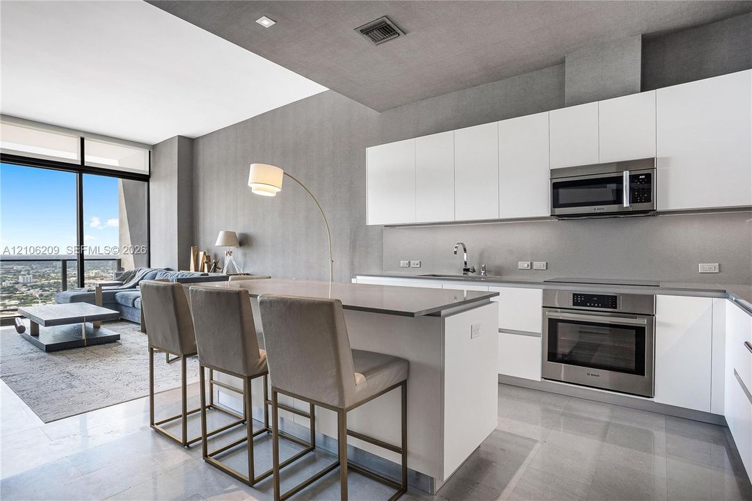 Modern kitchen featuring white flat-panel cabinetry, a central island with a solid-surface countertop, stainless steel appliances, and tile flooring