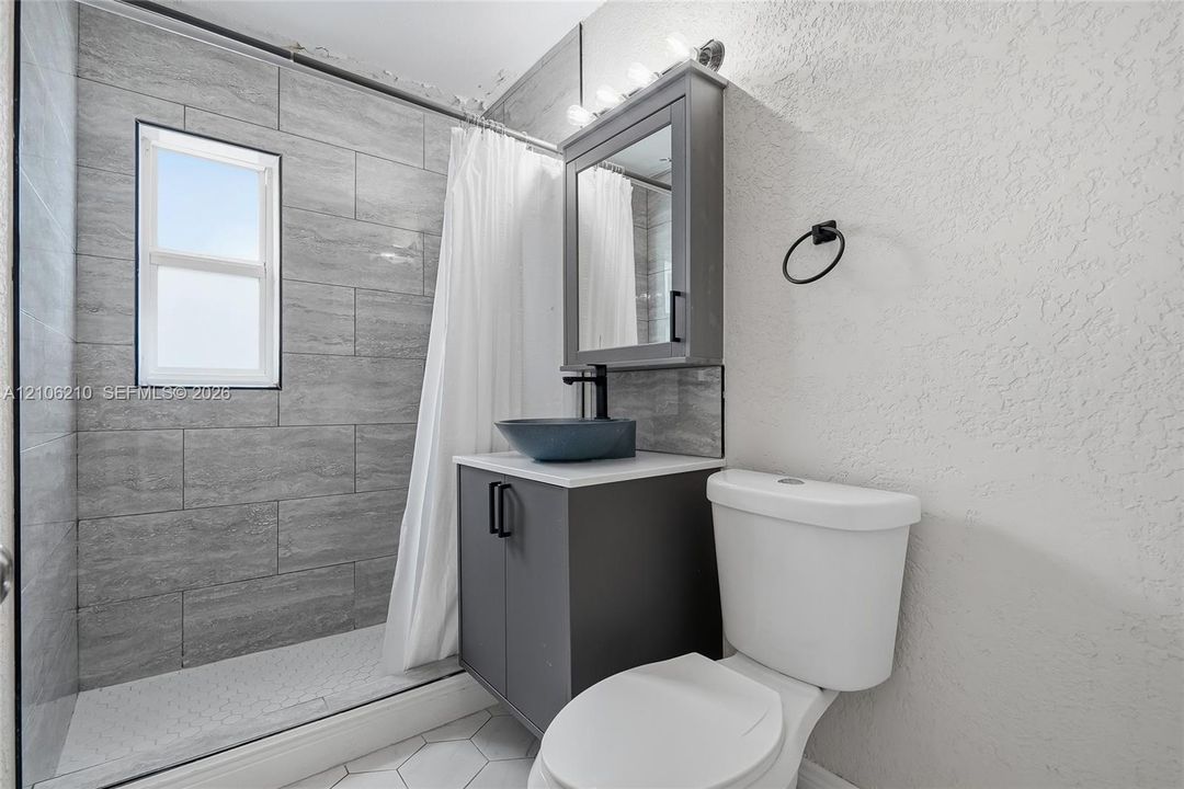 Bathroom featuring a walk-in shower with grey horizontal tile surround, grey vanity cabinet, vessel sink, and mirrored medicine cabinet