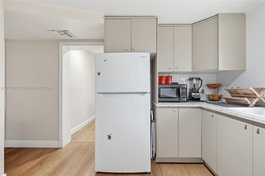 Kitchen featuring neutral-toned cabinetry, light-colored countertops, white subway tile backsplash, and wood-finish flooring
