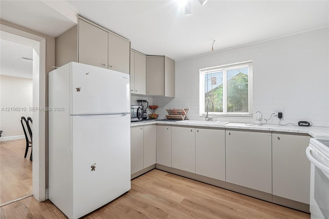 Kitchen featuring flat-panel cabinetry, stone-finish countertops, subway tile backsplash, stainless steel sink with gooseneck faucet, and wood-finish flooring