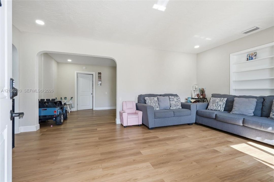 Living area featuring wood-finish flooring, recessed lighting, arched wall opening, and built-in white shelving