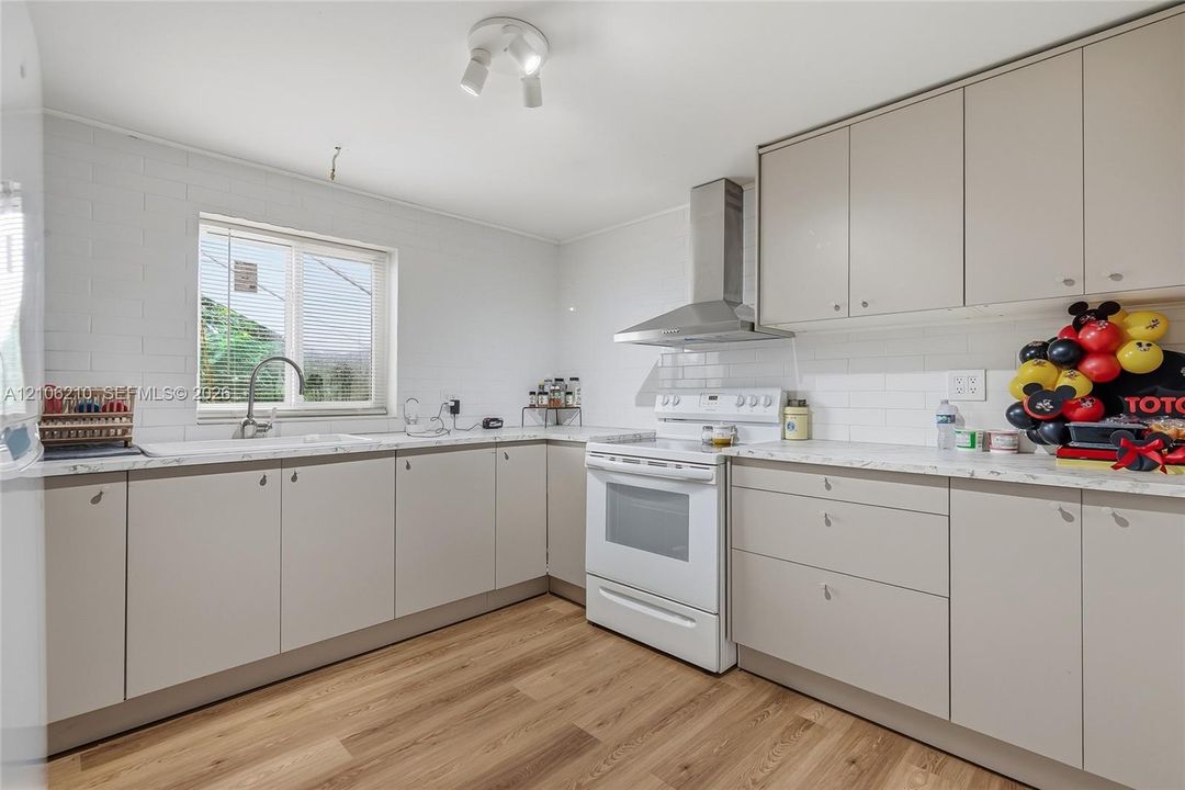 Kitchen featuring flat-panel cabinetry, stone-finish countertops, subway tile backsplash, stainless steel range hood, and wood-finish flooring