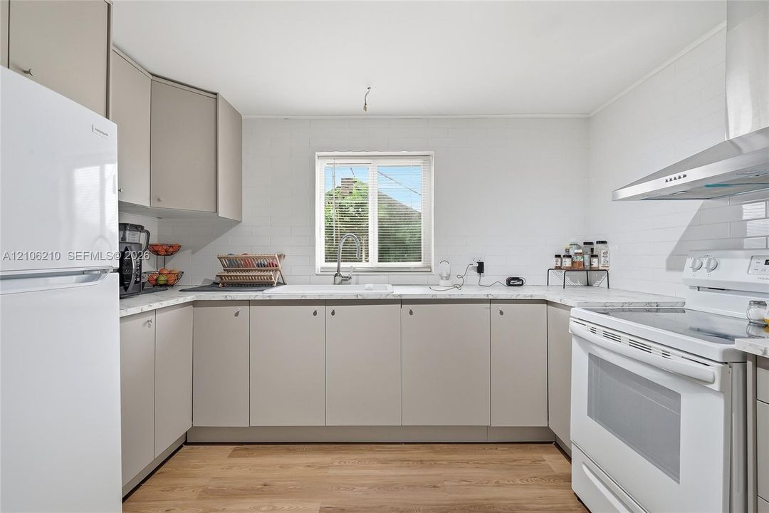 Kitchen featuring light gray flat-panel cabinetry, white solid surface countertops, a stainless steel range hood, and wood-finish flooring