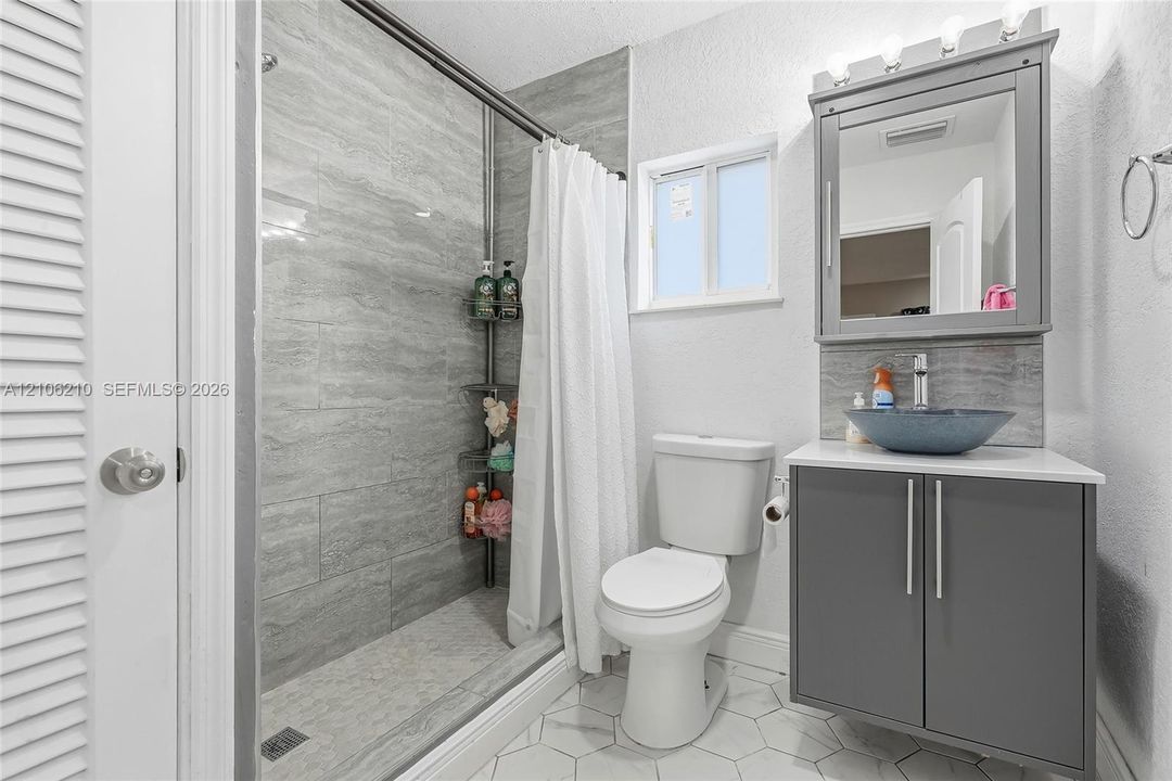 Bathroom featuring a shower stall with stone-finish tile surround, vanity with a vessel sink, integrated medicine cabinet, and white hexagonal floor tile
