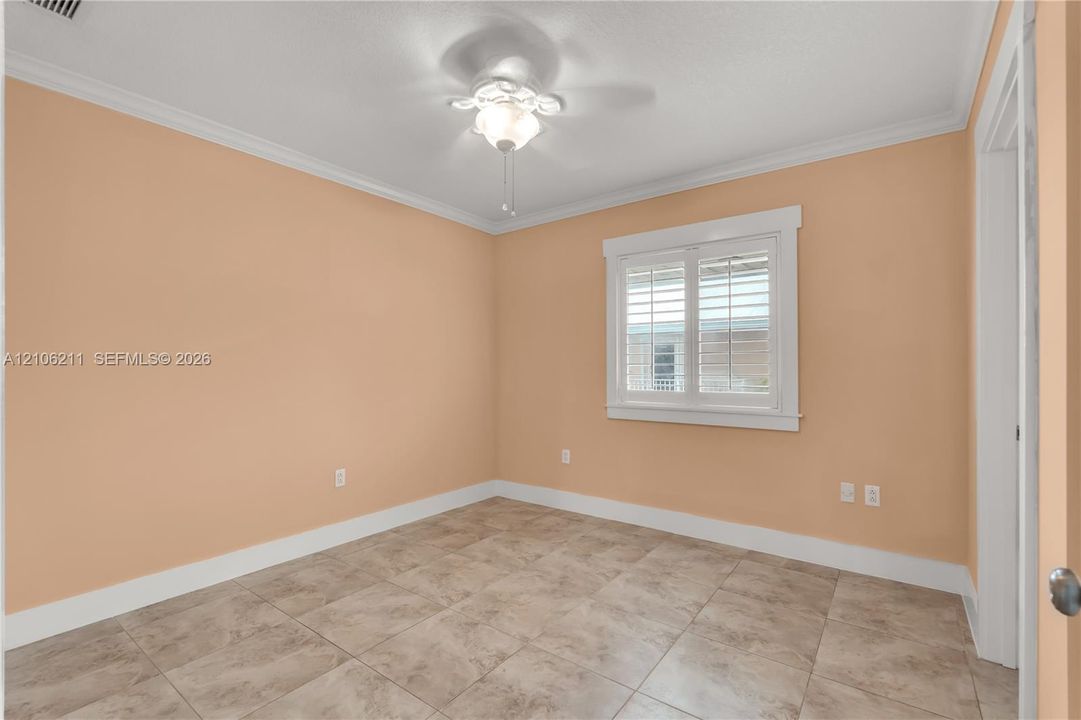 Room featuring neutral wall paint, large-format tile flooring, white crown molding, and plantation shutters